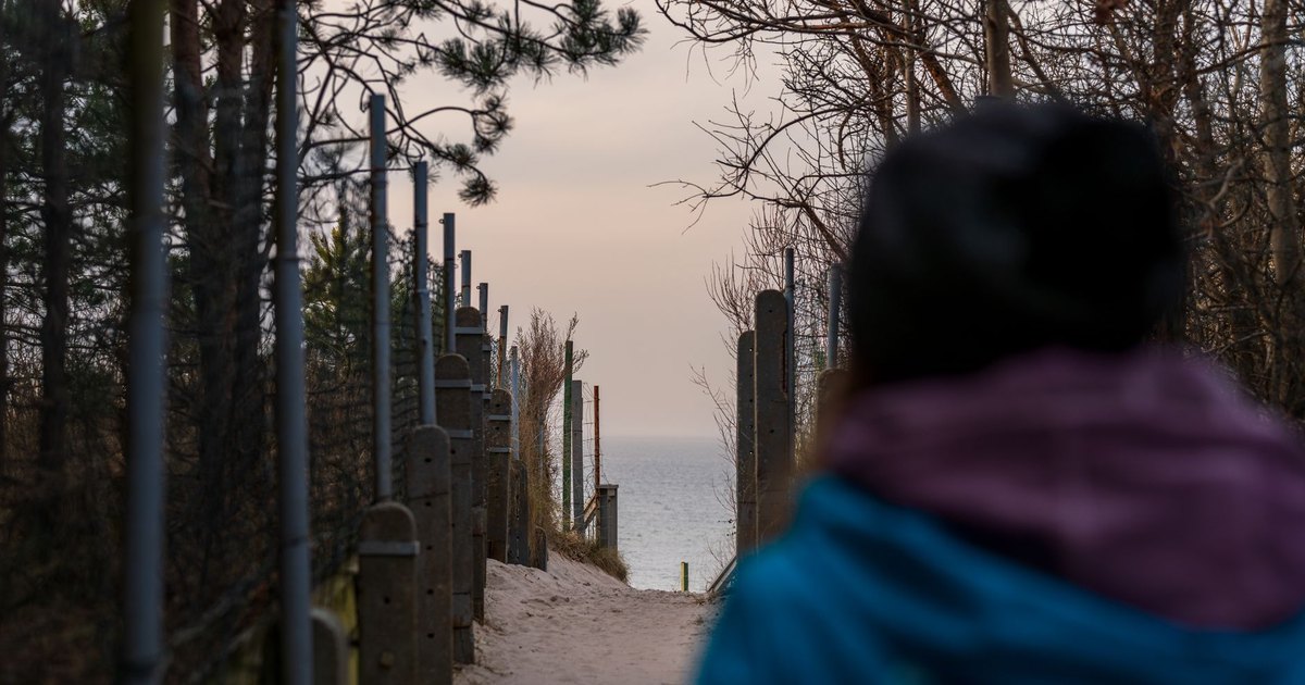 Migrants walking toward a border fence by the sea at dusk